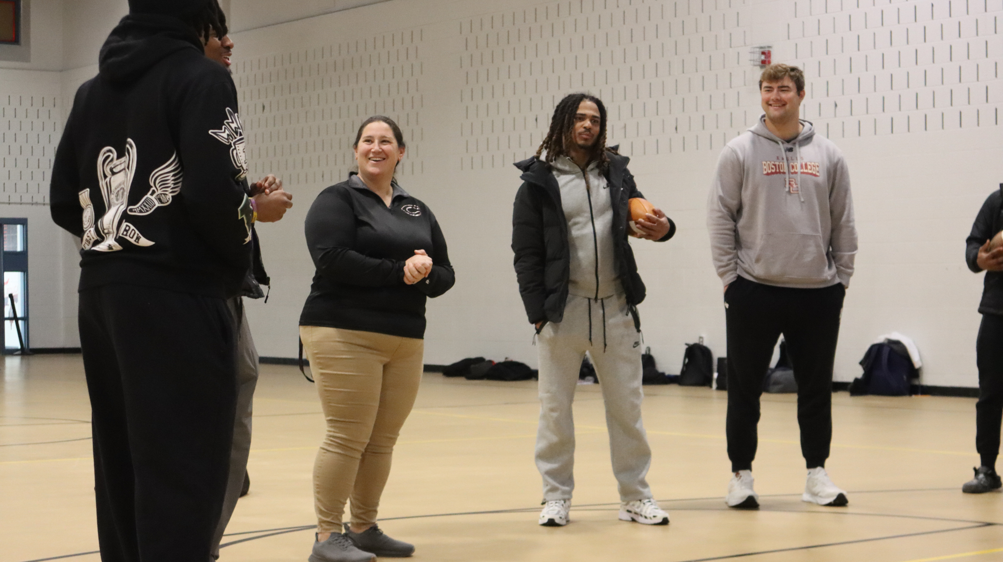 Members of the BC football team standing in the Blue Gymnasium at Chelsea High School speaking to CHS players